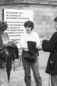Vor einem mehrsprachigen Schild zu ehemaligen Folterzellen der geheimen Staatspolizei stehen sechs Personen und scheinen sich über den historischen Ort auszutauschen.