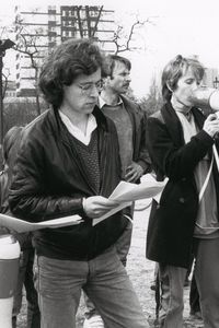 Eine Frau spricht durch ein Megafon. Links von ihr zwei Männer, einer mit gesenktem Megafon. Rechts ein weiterer Mann. Alle halten Zettel, auf die sie teils blicken. Die Stimmung ist konzentriert.